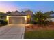 Inviting home exterior featuring a two-car garage, illuminated entryway, and lush landscaping, captured during twilight at 235 Pima Trl, Groveland, FL 34736