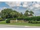 Welcoming community sign set amidst manicured hedges, palm trees, and lush greenery under a partly cloudy sky at 6250 Sailboat Ave, Tavares, FL 32778