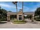 Community gated entrance with stone pillars, palm trees, manicured landscaping, and controlled access at 8682 Bridgeport Bay Cir, Mount Dora, FL 32757