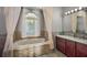 Relaxing bathroom with soaking tub under arched window and vanity with marble countertop at 10606 Masters Dr, Clermont, FL 34711