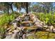 Landscaped backyard features a beautiful rock waterfall with lush ferns, plants, and trees surrounding the peaceful oasis at 1312 Patrick Pl, The Villages, FL 32162