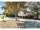 Wide angle exterior of a tan raised stilt home with mature trees in the front yard at 6490 Se 180Th Avenue Rd, Ocklawaha, FL 32179