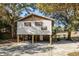 Exterior of a tan raised stilt home surrounded by mature trees, gravel yard and stairs at 6490 Se 180Th Avenue Rd, Ocklawaha, FL 32179