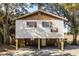 Exterior shot of stilt home with tan siding, brown shutters, basketball hoop and surrounded by mature trees at 6490 Se 180Th Avenue Rd, Ocklawaha, FL 32179