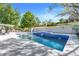 Backyard pool area featuring blue tile waterfall and lounging areas surrounded by green landscaping and a privacy wall at 12802 Amber Ave, Clermont, FL 34711