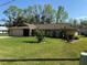 Well maintained lawn and mature landscaping enhance this single-story home with tan siding and brown roof at 5 Magnolia Ln, Yalaha, FL 34797