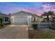 A home featuring a brick paved driveway leading to a one-car garage set against a colorful dusk sky at 9312 Se 172Nd Wayside Pl, The Villages, FL 32162