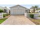 A home featuring a brick-paved driveway leading to a one-car garage and meticulously kept landscaping at 9312 Se 172Nd Wayside Pl, The Villages, FL 32162