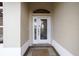 A close-up of a white front door featuring decorative glass and a transom window, set within a neutral-colored entryway at 3234 Berkeley Ln, The Villages, FL 32162