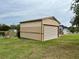 A well-maintained, tan metal garage that has a horizontal rolling garage door. There is ample lawn space around the garage at 12066 Se 60Th Avenue Rd, Belleview, FL 34420