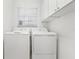 Well-lit laundry room with a side-by-side washer and dryer, a window, and overhead storage cabinets at 592 Juniper Way, Tavares, FL 32778