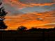 Striking orange sunset over a wide open fenced field; trees in silhouette at 8230 Se 23Rd Dr, Webster, FL 33597