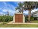 A tan-colored storage shed with double doors sits beside a large palm tree in the manicured yard at 12338 S Putney Ct, Leesburg, FL 34788