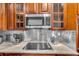 Modern kitchen featuring stainless steel microwave, tile backsplash, wooden cabinets, and granite countertops at 6240 Tremayne Dr, Mount Dora, FL 32757