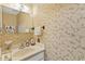 Powder room featuring a vanity with a white sink, classic wallpaper, and decorative accents at 9906 County Road 114A, Wildwood, FL 34785