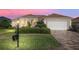 Charming single-story home featuring a well-manicured lawn, a two-car garage and tropical landscaping at dusk at 12239 Se 92Nd Court Rd, Summerfield, FL 34491
