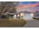 Sunset view of a single-story home featuring a well-manicured lawn and a two-car garage at 2136 Kerwood Loop, The Villages, FL 32162