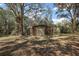 View of an outbuilding with a roll-up door in a wooded, grassy lot with mature trees at 2541 Lake Griffin Rd, Lady Lake, FL 32159