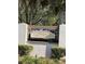 Community sign that reads Villa De Leon surrounded by manicured shrubs under mature trees at 2606 Olivarez Way, The Villages, FL 32162