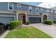 Exterior view of blue townhomes featuring a paver driveway, garages, manicured landscaping and red front doors at 384 Coral Beach Cir, Casselberry, FL 32707