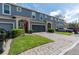 Exterior view of blue townhomes featuring a paver driveway, garages, manicured landscaping and red front doors at 384 Coral Beach Cir, Casselberry, FL 32707