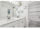 Bright bathroom featuring dual sinks, white cabinets, a large mirror and tiled shower at 5509 Windsong Oak Dr, Leesburg, FL 34748