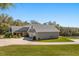 Rear view of a gray home featuring an attached three-car garage and lush landscaping at 2600 Robie Ave, Mount Dora, FL 32757