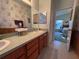 Well-lit bathroom featuring a double sink vanity with wood cabinets and a decorative wallpaper, leading into the bedroom at 25124 Twelve Oaks Rd, Leesburg, FL 34748