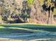 Close-up of a putting green with a sand trap in the foreground, mature trees and shrubs in the background at 25124 Twelve Oaks Rd, Leesburg, FL 34748