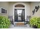 Charming front porch featuring rocking chairs, decorative plants, and a stylish front door with glass panels at 3426 Boardroom Trl, The Villages, FL 32163