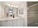 Bathroom featuring double vanity, white cabinets, large mirror, and glass-enclosed shower at 613 Sherwood St, The Villages, FL 32162