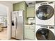 Efficient laundry area with stacked washer/dryer, stainless fridge, and sink with sage green cabinetry at 7885 Se 166Th Hibernia Ln, The Villages, FL 32162