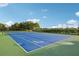 Immaculate community tennis court with a blue surface, surrounded by lush landscaping and a fence at 909 Egrets Landing Way, Groveland, FL 34736