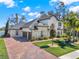 Elegant exterior of home with a brick driveway, manicured lawn, arched entryway, and a three-car garage at 9513 Mid Summer Ln, Leesburg, FL 34788