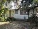 Exterior of a weathered white house featuring a front door, windows, and overgrown vegetation at 100 Palm St, Fruitland Park, FL 34731