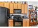 Well-lit kitchen with black appliances, wood cabinets, and black countertops and an adjacent wooden display cabinet at 112 Flame Vine Way, Groveland, FL 34736