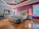 Spacious bedroom features mirrored furniture, a gray upholstered bed, a tray ceiling, and hardwood floors at 17694 Se 88Th Covington Cir, The Villages, FL 32162
