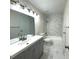 Bathroom featuring a gray vanity with a white countertop, framed mirror, toilet, and a shower with white marble-patterned tile at 18203 Sandalwood Dr # 18203, Wildwood, FL 34785