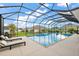 Screened-in pool area featuring a pool, waterfall feature, lounge chairs and lush landscaping at 712 Krietemeyer Path, The Villages, FL 32163