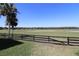 A serene view of a grassy backyard that stretches to a wetland area, bordered by a classic black wooden fence at 1215 Eagle Ridge Dr, The Villages, FL 32162