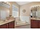 Well-lit bathroom boasting a garden tub, glass block window, and and vanities with marble countertops at 13800 Wellington Ln, Grand Island, FL 32735