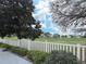 Picturesque view of a golf course features lush green grass, mature trees, and a classic white picket fence at 3285 Archer Ave, The Villages, FL 32162