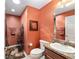 Bathroom with earthy orange walls, vanity, toilet, framed art and black metal shelving at 483 Cammarano Pl, The Villages, FL 32162