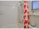 Fresh bathroom with tiled shower, tub, red flower shower curtain and storage shelf beside the toilet at 9188 Chandler Dr, Groveland, FL 34736