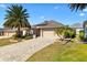 Charming home featuring a brick driveway, well-manicured lawn, and beautiful landscaping with palm trees at 1357 Owl Dr, The Villages, FL 32163