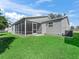 View of the backyard with well-maintained lawn, screened-in patio, exterior door, and AC unit at 17442 Se 79Th Lovewood Ave, The Villages, FL 32162