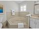 Bathroom featuring a tiled garden tub with neutral countertops, white cabinetry, and plantation shutters at 3400 Foxboro Ct, Mount Dora, FL 32757