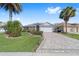 Home featuring a paved driveway and lush green lawn with palm trees at 565 Brighton Dr, The Villages, FL 32162