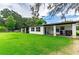 Back exterior featuring a white single-story home with a long covered porch, a lush lawn and mature tree at 132 E Belt Ave, Bushnell, FL 33513