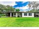 Rear exterior showcasing a white single-story house with a covered porch, well-maintained lawn, and serene backyard at 132 E Belt Ave, Bushnell, FL 33513